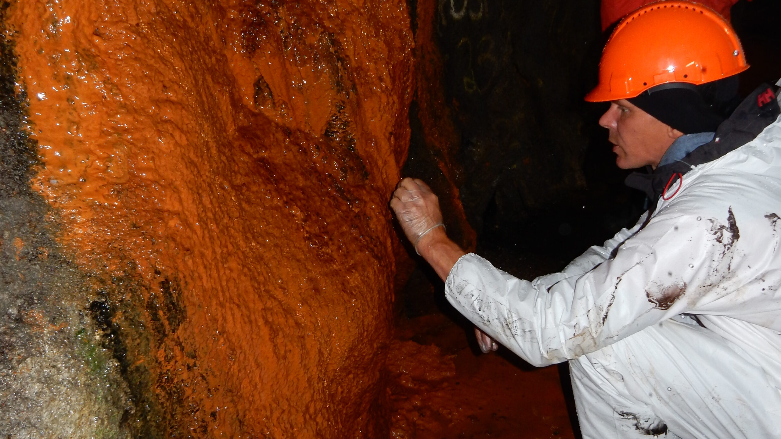 Inträngande havsvatten för med sig bakterier som bildar kolonier – biofilm. Bakterierna angriper den betong som ska förhindra att stenar lossar från tunnelväggarna. Betongen blir porös och riskerar att brytas sönder. Biofilmen får sin markanta färg av rostande armering i sprutbetongen.
